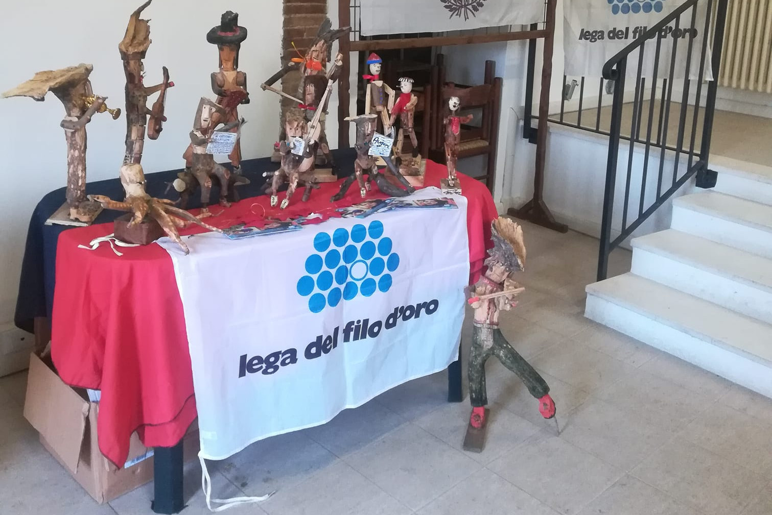 Nella foto c'è un tavolo coperto da una bandiera della lega del filo d'oro e sopra di esso sono appoggiate delle sculture di legno fatte a mano.