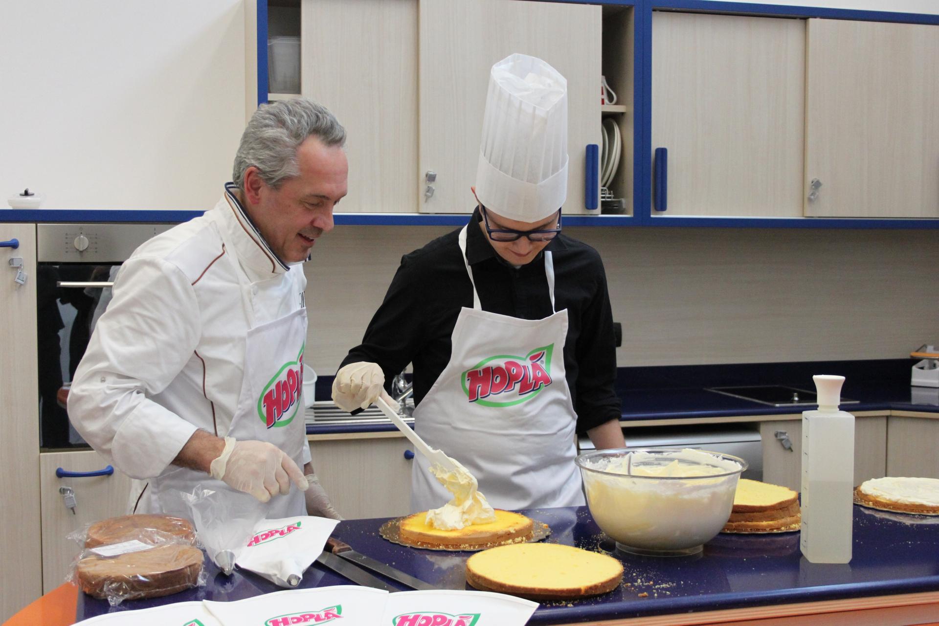 Un pasticcere nella cucina didattica (presso il Centro Nazionale della Lega del Filo d'Oro) con il nostro Victor, prepara insieme a lui delle torte di pan di Spagna decorandole con la panna montata Trevalli. Victor indossa un cappello da chef e sta deponendo la panna sulla torta con un cucchiaio