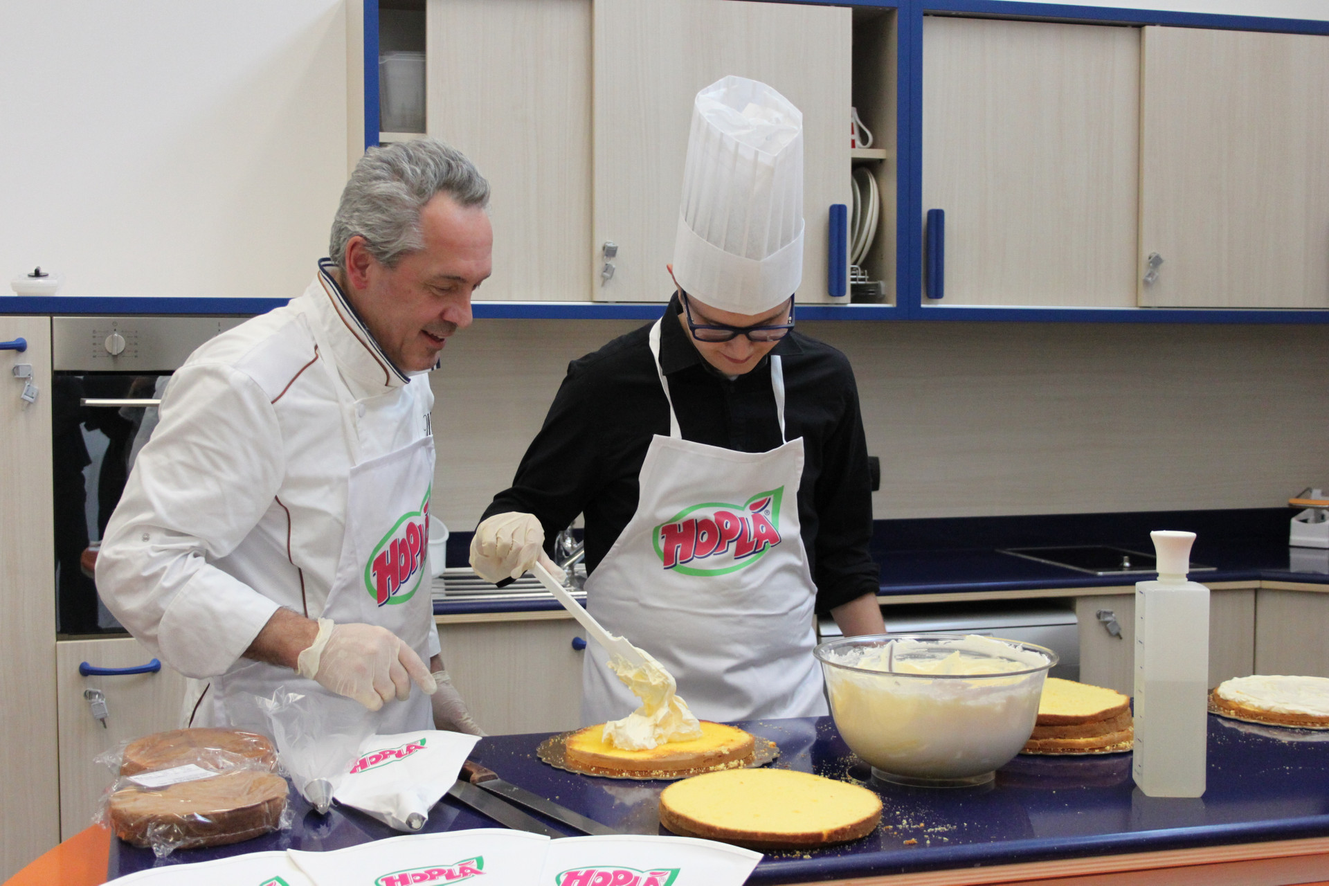 Un pasticcere nella cucina didattica (presso il Centro Nazionale della Lega del Filo d'Oro) con il nostro Victor, prepara insieme a lui delle torte di pan di Spagna decorandole con la panna montata Trevalli. Victor indossa un cappello da chef e sta deponendo la panna sulla torta con un cucchiaio