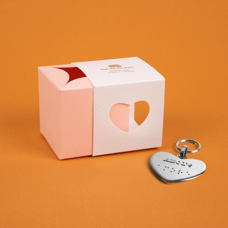 Bomboniera composta da due scatoline in cartoncino pregiato inserite l'una nell'altra. Quella esterna è bianca, quella interna, visibile da un'apertura a forma di cuore, è rosa. Accompagnata dal suo portachiavi cuore