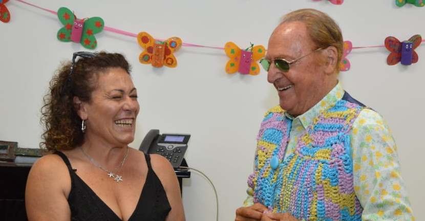 Renzo Arbore felice in visita alla sede di Napoli riceve in dono da Matilde, sorridente ed emozionata, un colorato gilet realizzato a mano da lei. Accanto ad Arbore è presente anche il Presidente Rossano Bartoli che sorride.