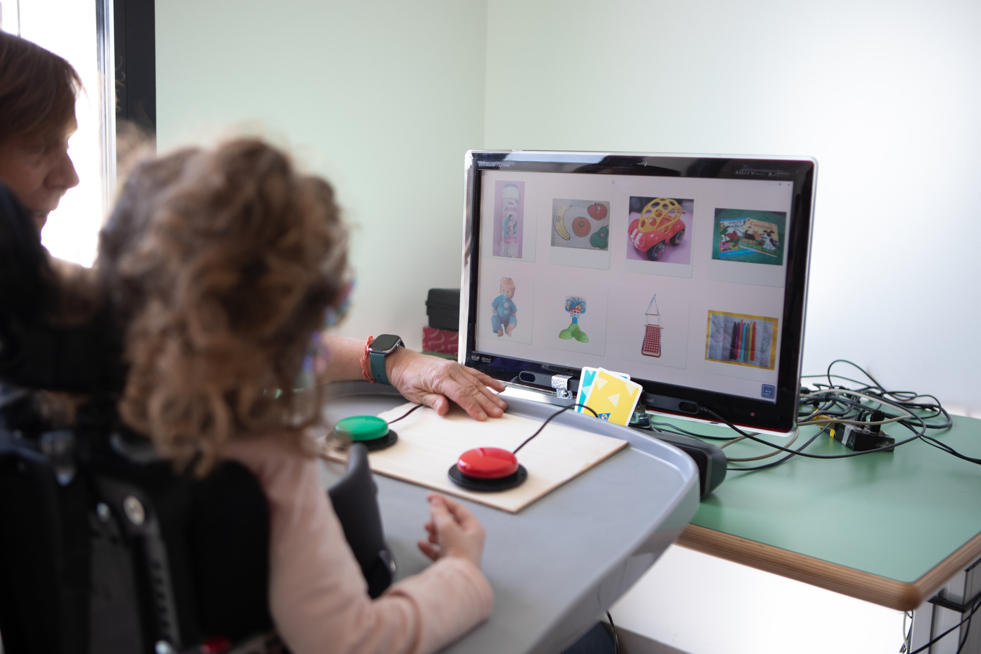 Melissa sta usando gli Switch e i V.O.C.A., dei pulsantoni colorati che le permettono di esprimere le proprie scelte, o di azionare un vocalizzatore per dire "Sì" e "No", sfruttando quei piccoli movimenti delle mani che Melissa riesce a controllare