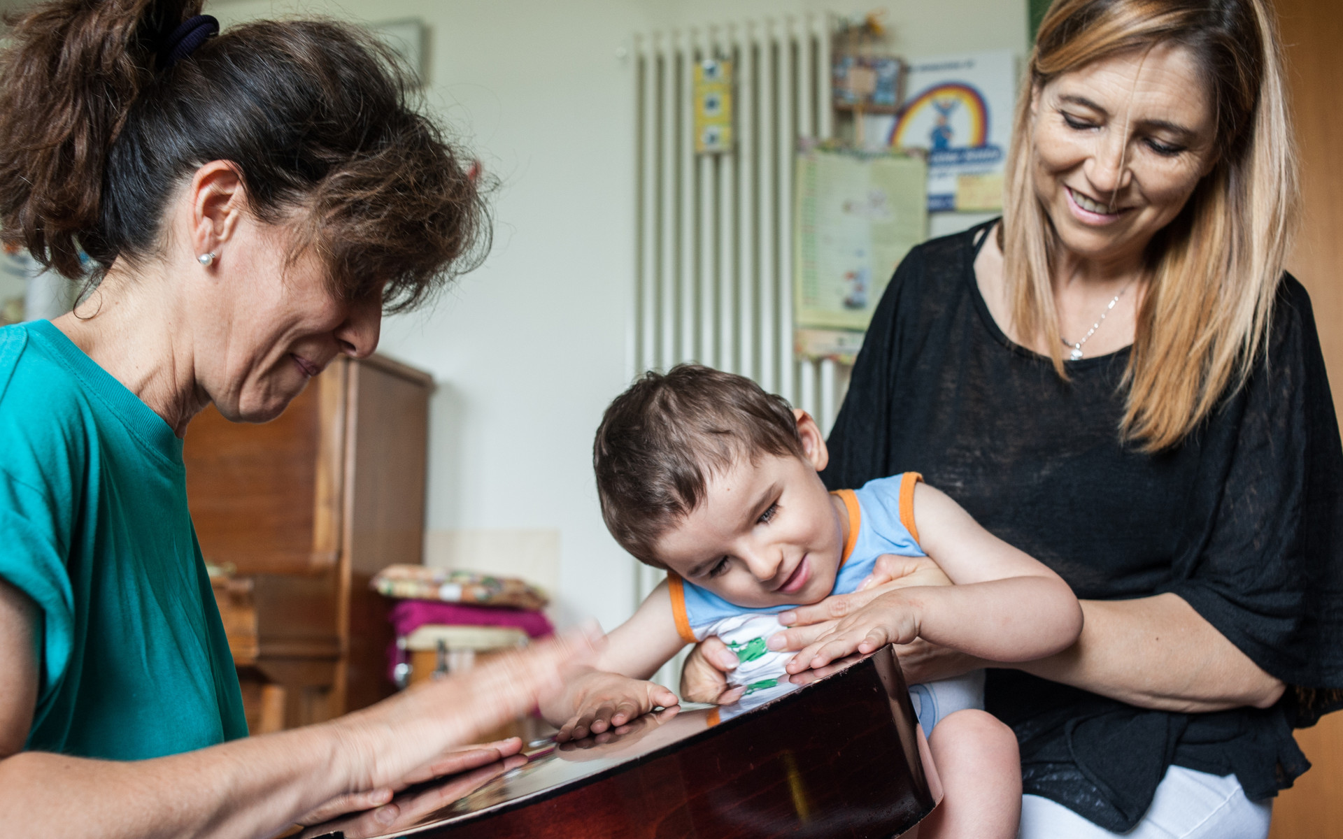 Fiammetta Musicoterapista del Centro di Osimo, batte le mani sulla cassa armonica di una chitarra per il piccolo Niccolò, che avverte le vibrazioni con le mani e sorride, tenuto in braccio dalla sua educatrice Teresa Anna.