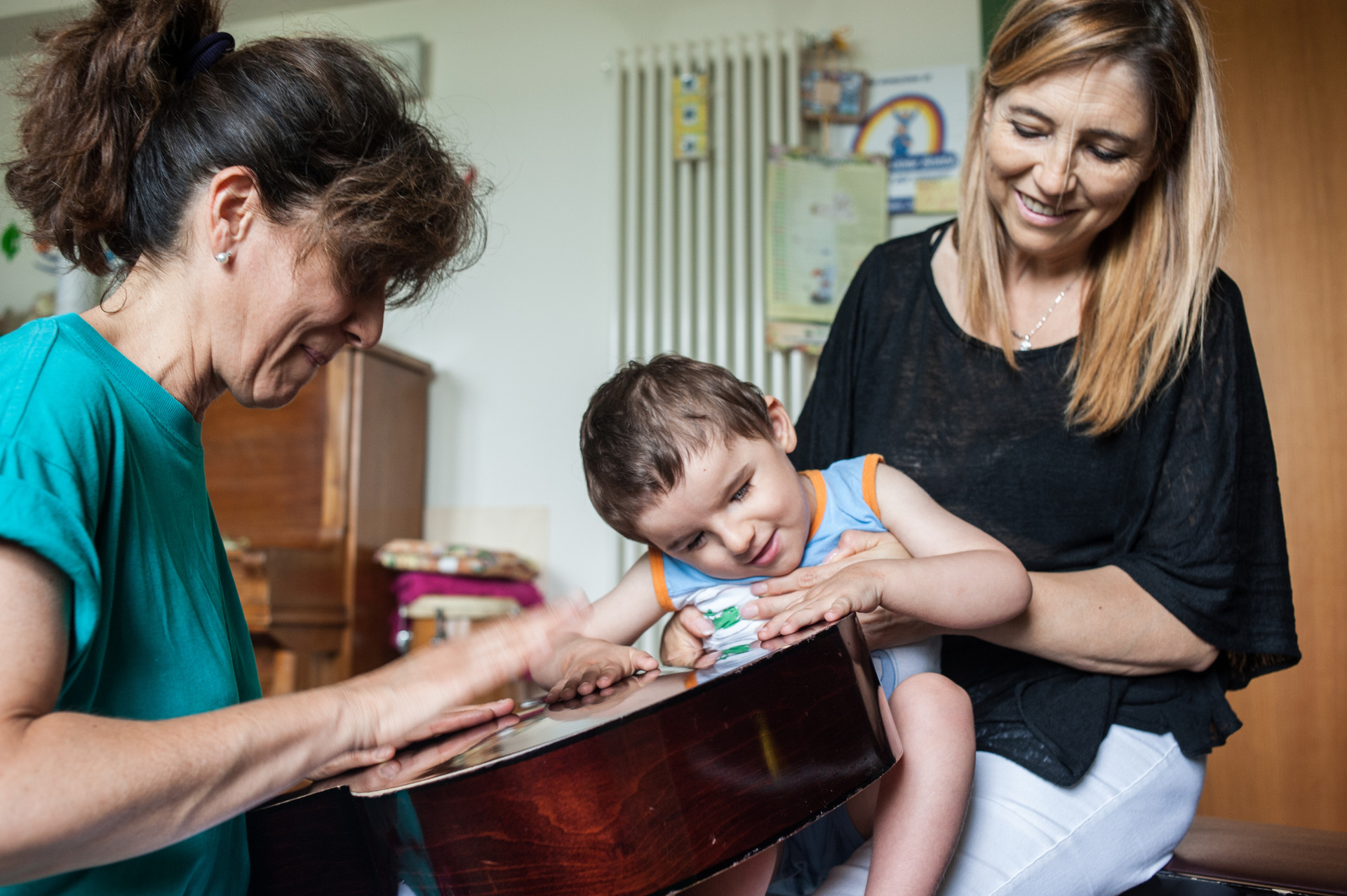 Fiammetta Musicoterapista del Centro di Osimo, batte le mani sulla cassa armonica di una chitarra per il piccolo Niccolò, che avverte le vibrazioni con le mani e sorride, tenuto in braccio dalla sua educatrice Teresa Anna.