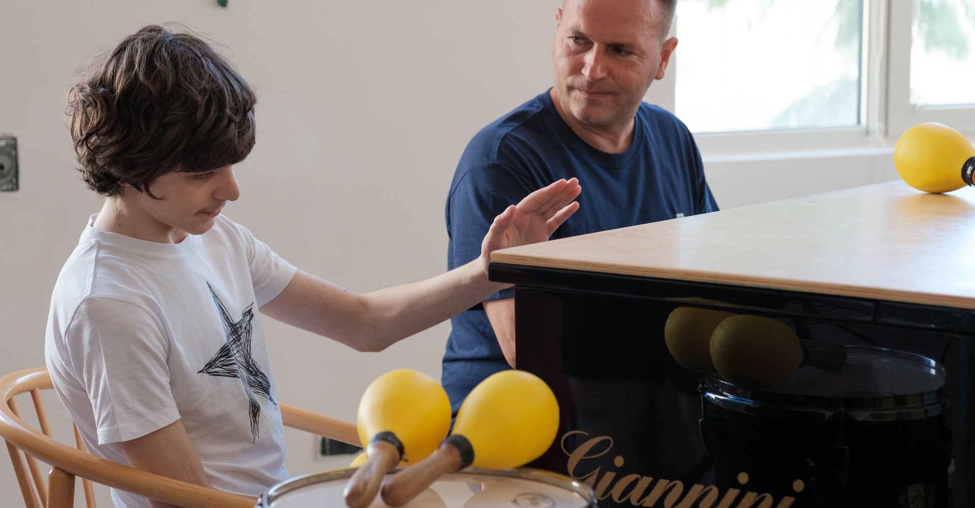 Francesco, un utente adolescente della Lega del Filo d'Oro che fa musicoterapia, vicino a un pianoforte a coda nero, circondato da maracas e tamburi