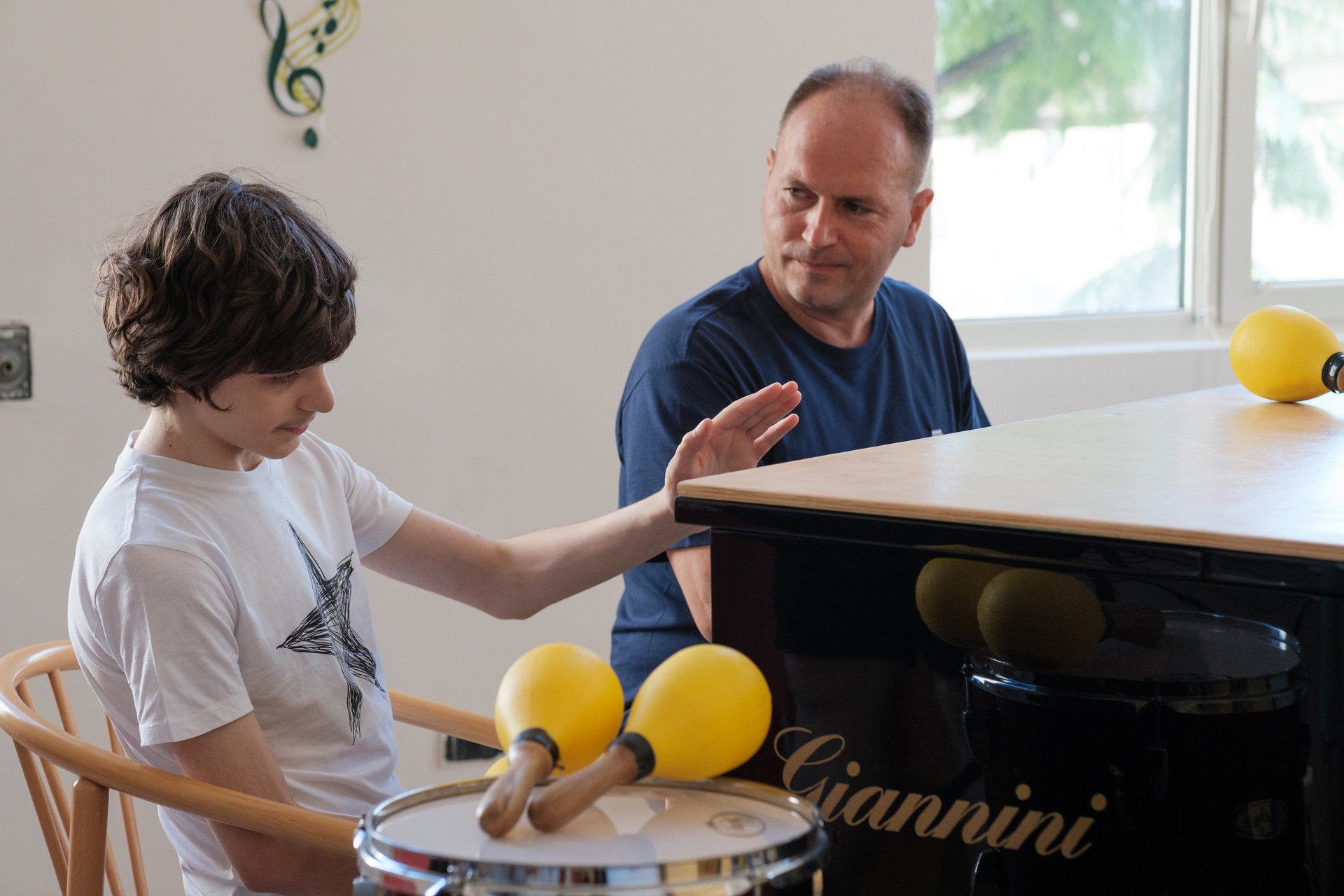 Francesco, un utente adolescente della Lega del Filo d'Oro che fa musicoterapia, vicino a un pianoforte a coda nero, circondato da maracas e tamburi
