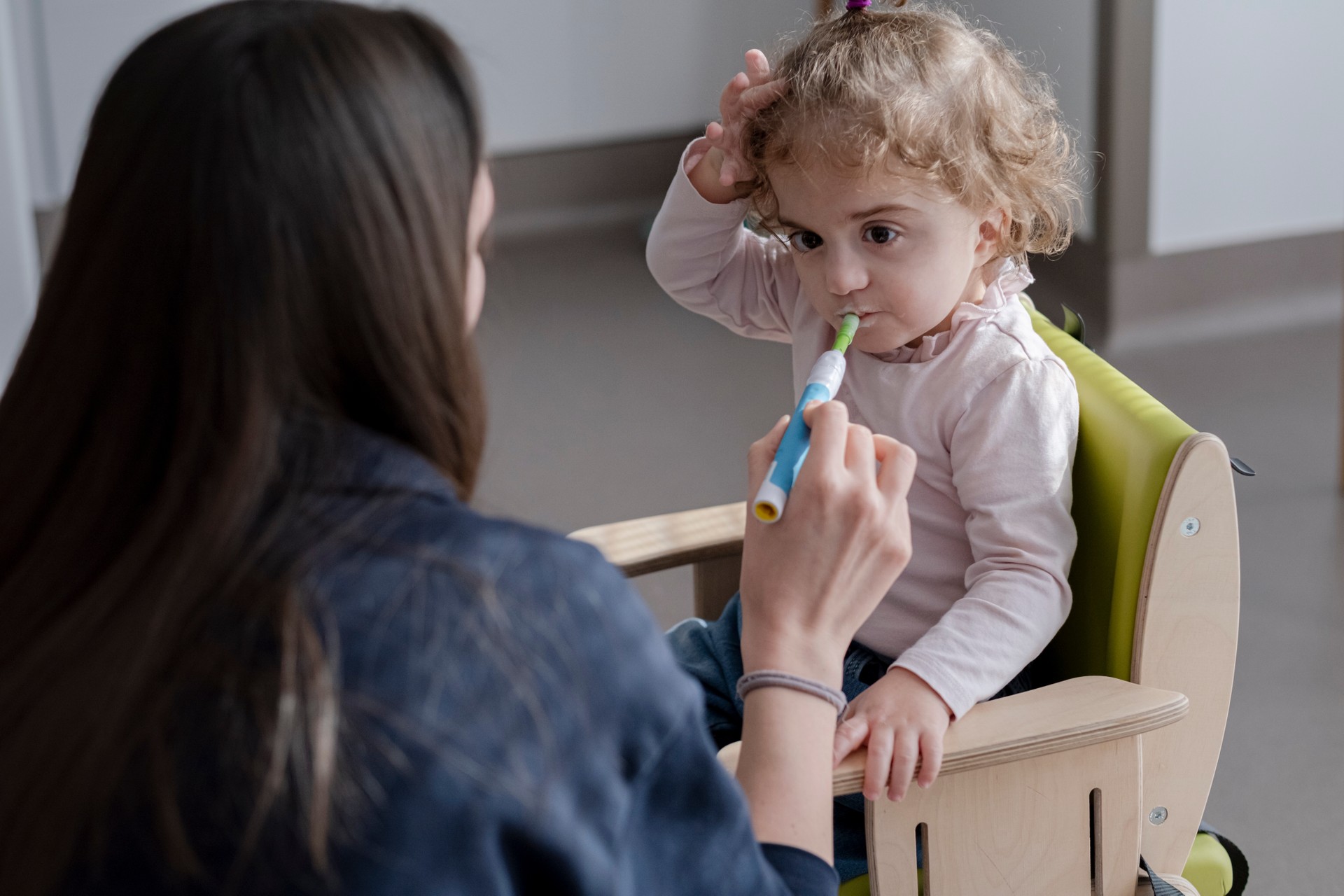 Benedetta è seduta su una sedia di legno e, tramite l'ausilio di un bastoncino colorato, sta facendo esercizi per la masticazione e deglutizione insieme alla sua educatrice