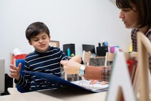 Agostino mentre gioca con la sua educatrice, sfogliano il quadernone delle attività. Agostino sorride