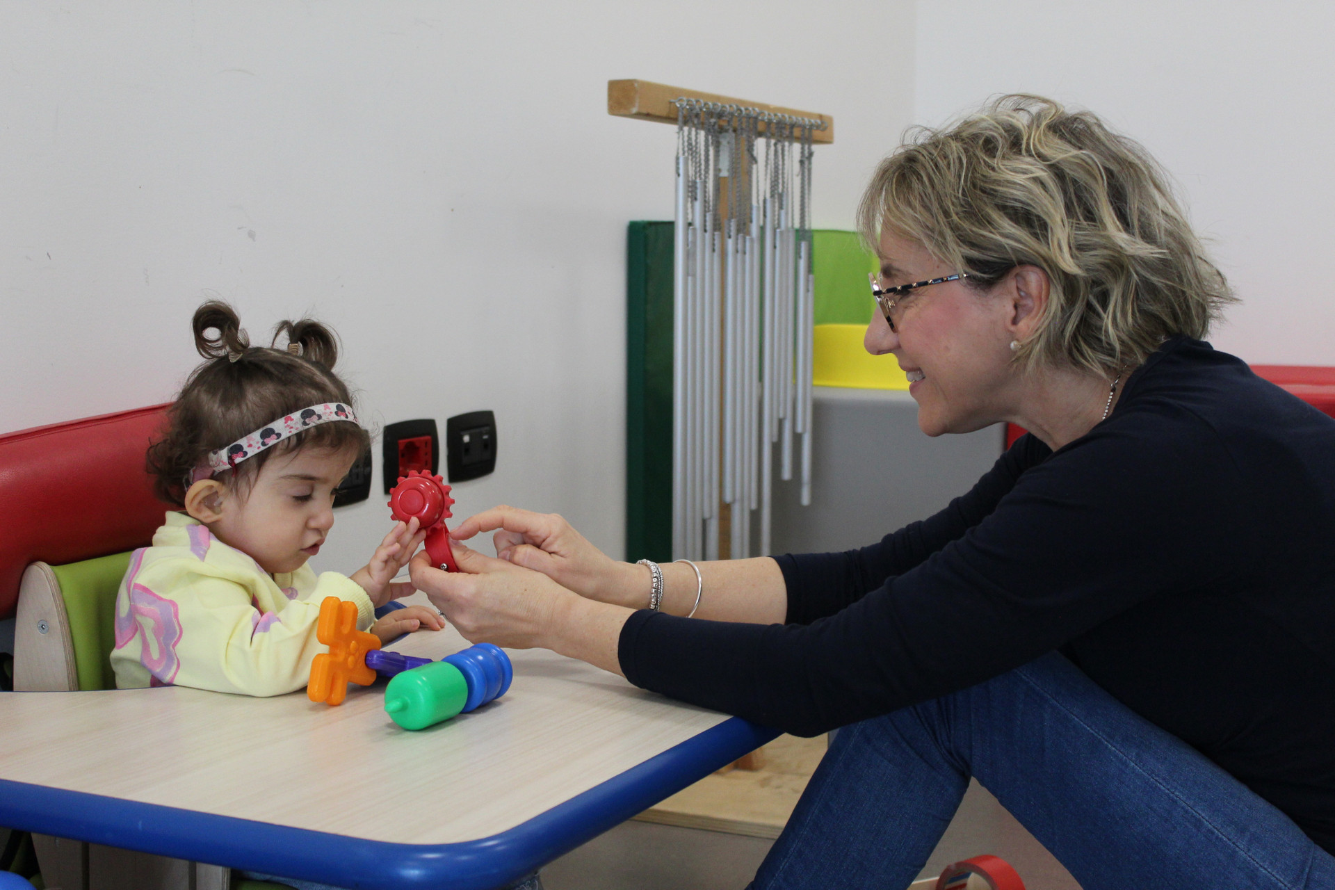 Seduta di musicoterapia. Sophie, una bambina sordocieca di circa 3 anni è seduta ad un piccolo tavolino e gioca con Manola, l'educatrice
