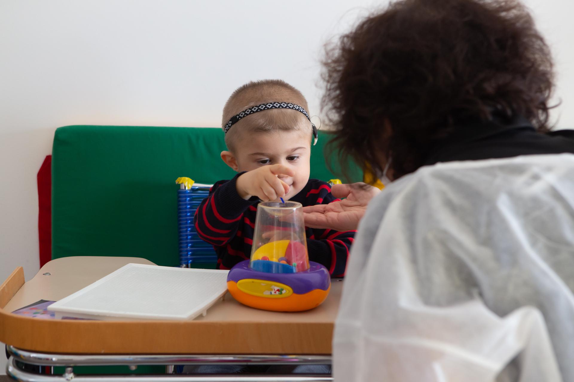 Il piccolo Berk, ospite del Centro Diagnostico, fa un'attività educativo-riabilitativa con l'educatrice con l'aiuto di un giocattolo colorato