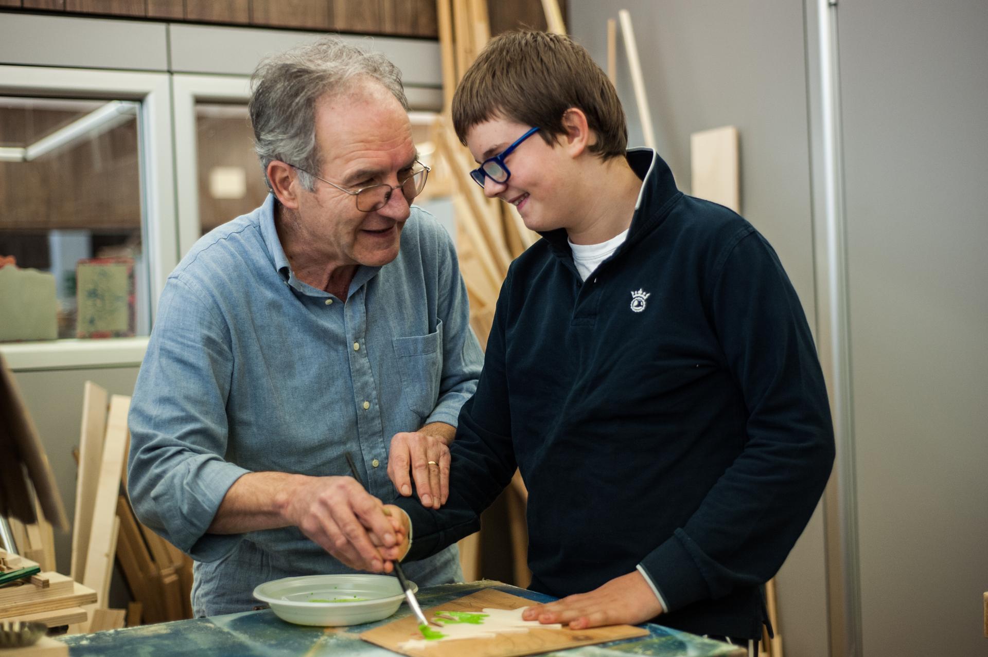 Un volontario chiacchiera con Victor un utente della Lega del Filo d'Oro di Osimo. Mentre il ragazzino dipinge col pennello una decorazione natalizia l'anziano volontario lo aiuta tenendogli il braccio e la mano