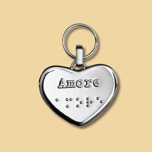 Portachiavi in metallo su sfondo giallo. Il charm è a forma di cuore piatto, su questo lato si legge la scritta "Amore" in Braille e stampatello 41