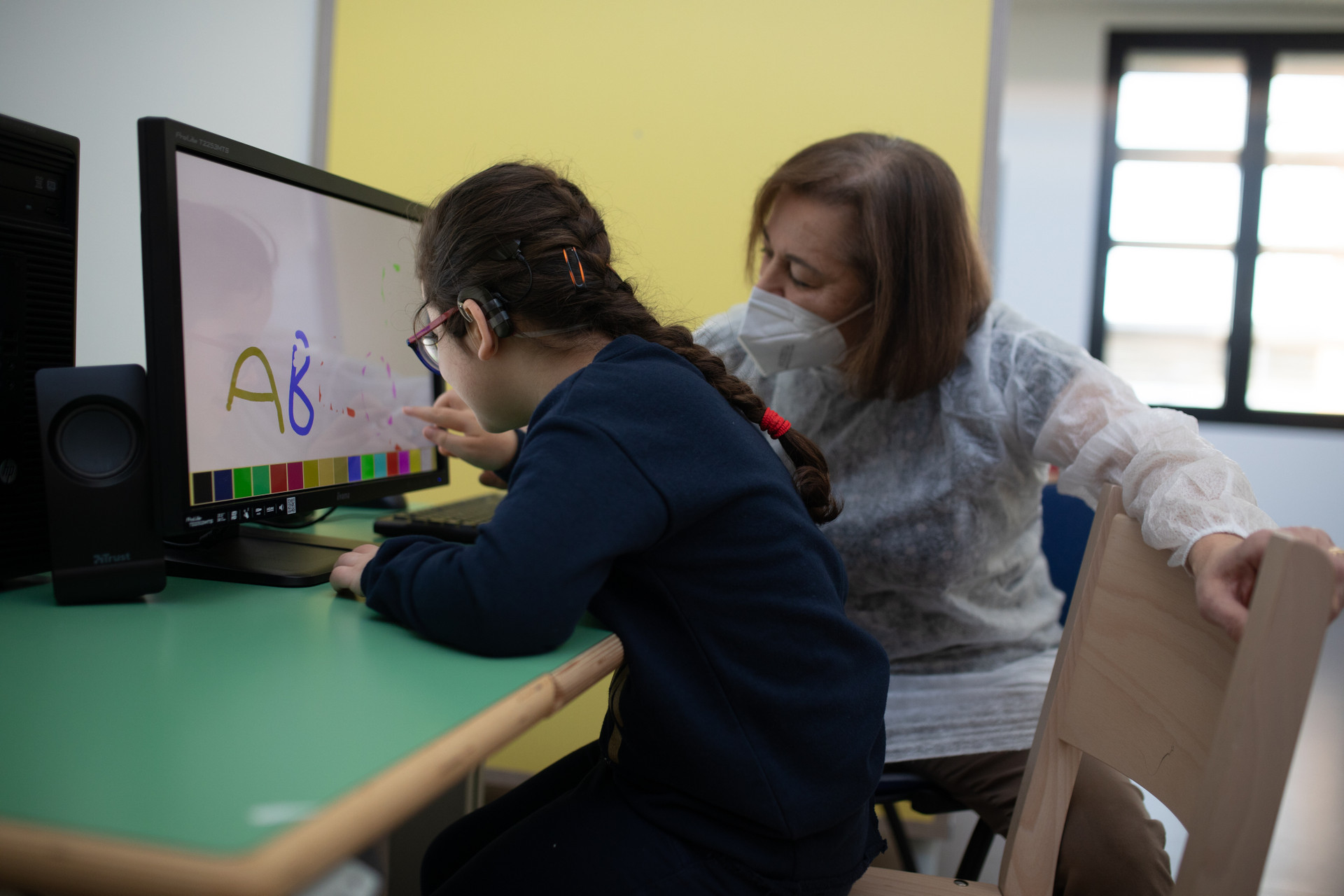 Una bambina della Lega del Filo d'Oro è intenta a svolgere un'attività davanti a un monitor insieme a un'operatrice.