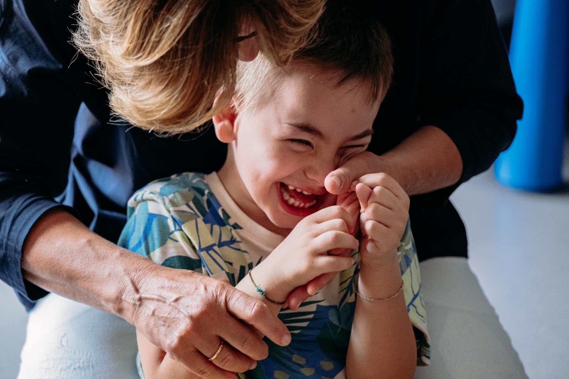 L'educatrice Loretta gioca insieme a Edoardo, bimbo seguito dalla Lega del Filo d'Oro. Nella foto si vede Edoardo in primo piano che ride felice mentre Loretta si chia su di lui.