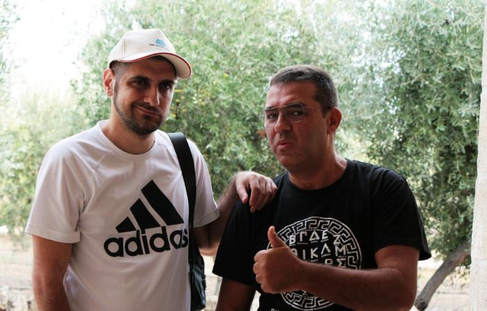 I due ragazzi posano felici, indossano magliette a maniche corte e alle loro spalle si intravedono degli alberi 