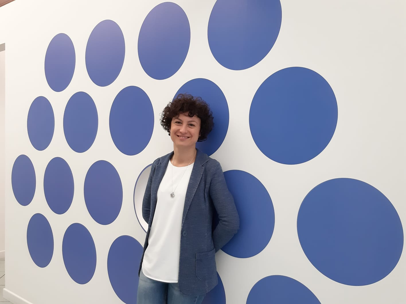Eleonora è sorridente ed è appoggiata con le mani dietro la schiena ad una parete su cui è impresso il logo della Lega del FIlo dìOro.