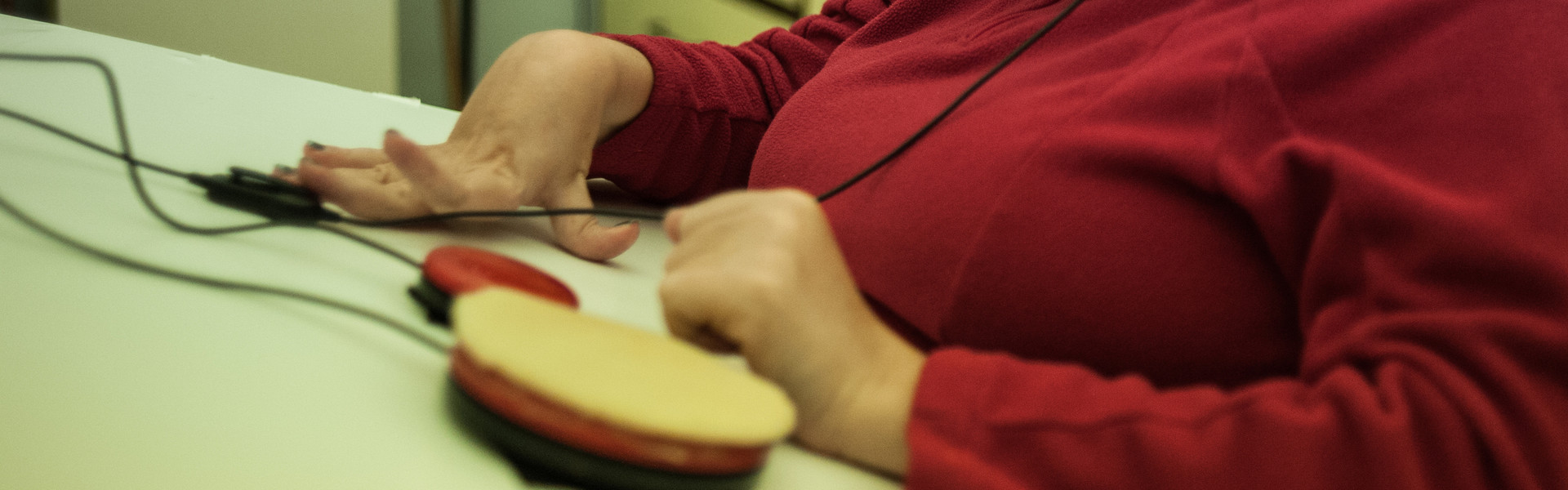 Paola, utente adulta del Centro di Osimo, sta usando un ausilio tecnologico. Si tratta di un pulsante switch, connesso a un sintetizzatore vocale, con cuffie e microfono