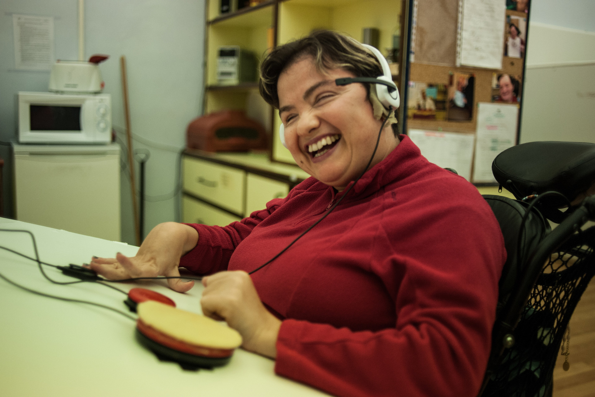 Paola, utente adulta del Centro di Osimo, sta usando un ausilio tecnologico. Si tratta di un pulsante switch, connesso a un sintetizzatore vocale, con cuffie e microfono