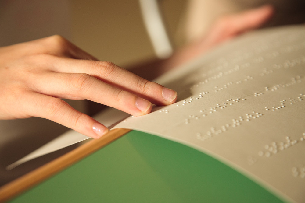 Dettaglio di mani che leggono un foglio scritto in Braille
