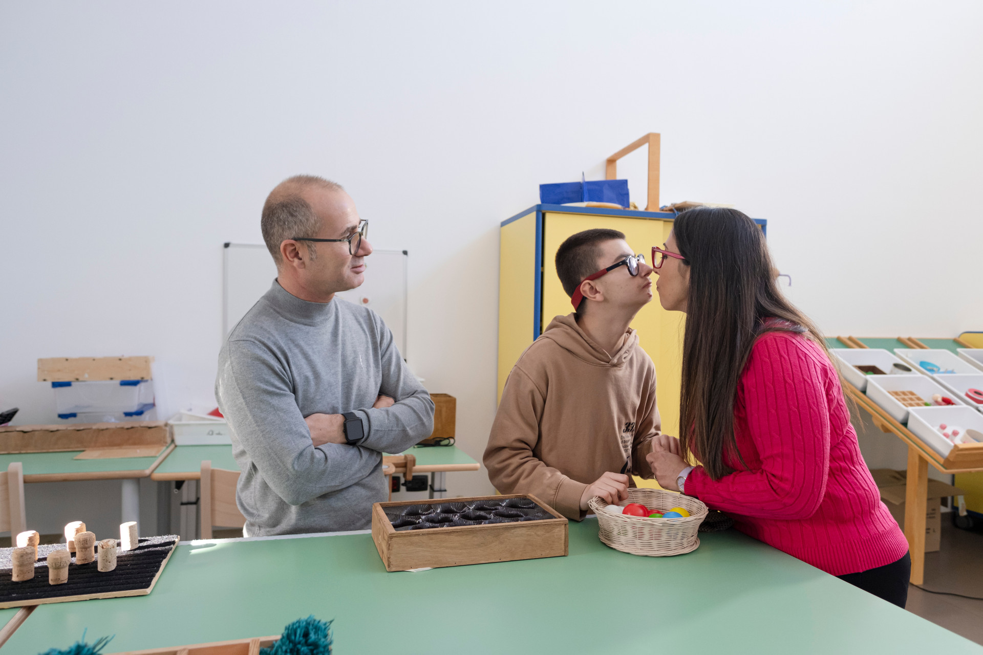 Biagio Luigi, ragazzo seguito dalla Lega del Filo d'Oro, in un'aula del Centro Nazionale con i suoi genitori. Nella foto giocano Luigi sta per dare un bacino alla mamma