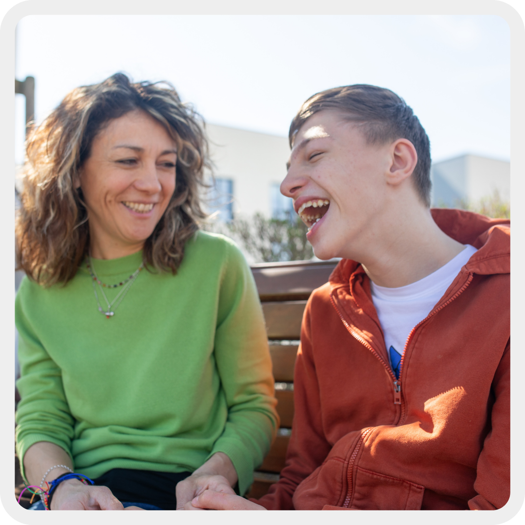 Filippo, ragazzo seguito dalla Lega del Filo d'Oro, insieme alla mamma Valentina sono seduti su una panchina del Centro Nazionale e ridono moltissimo divertiti.