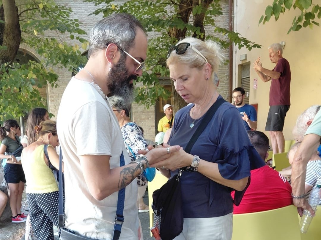 Fotografia scattata durante il soggiorno estivo nelle Marche organizzato dalla Lega del Filo d’Oro. In uno spazio all’aperto, un uomo e una donna comunicano tramite lo stampatello sulla mano: una traccia lettere sul palmo dell’altra.