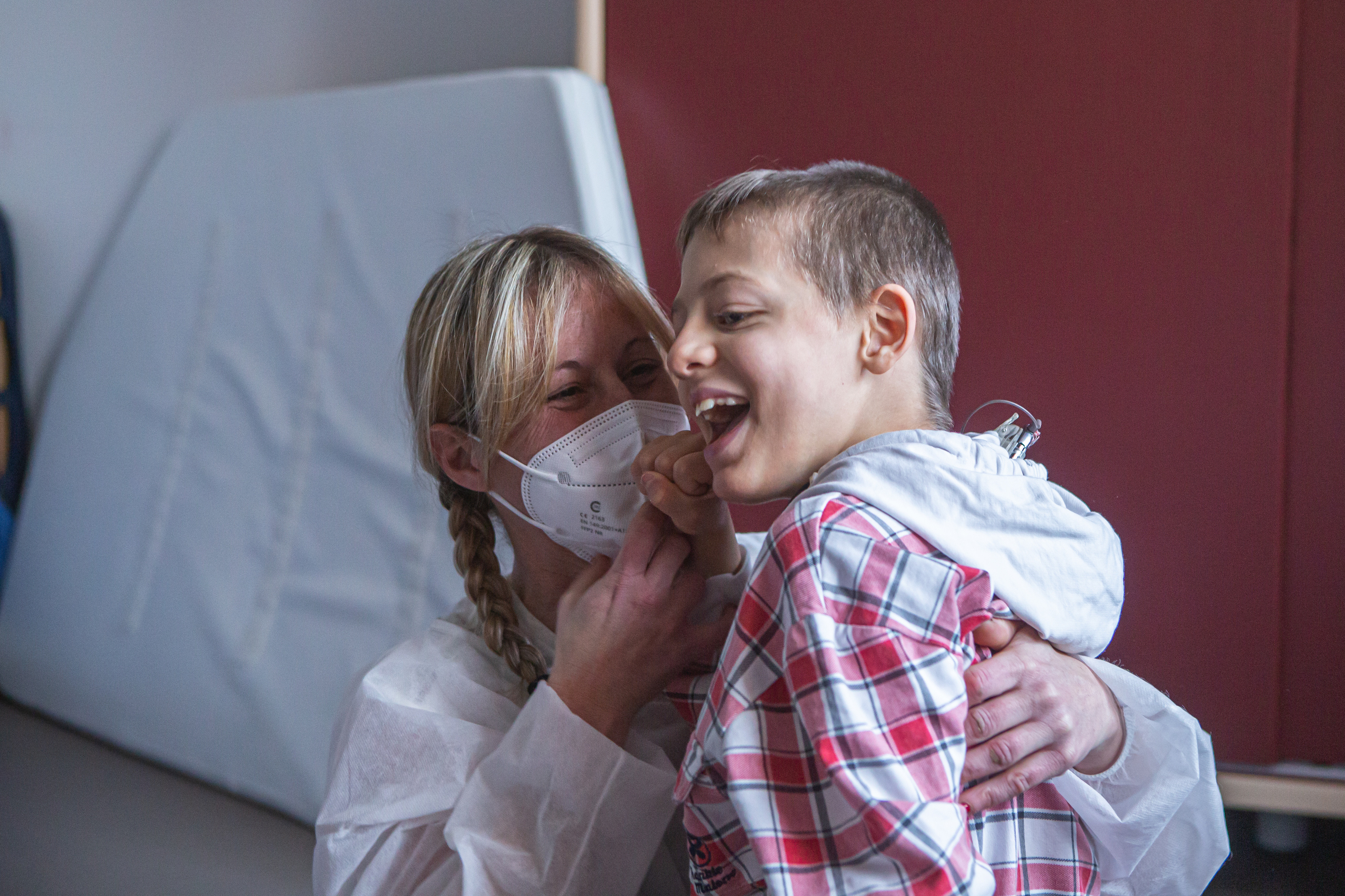 Matteo, piccolo utente del Centro di Osimo, ride con la sua educatrice che lo abbraccia. L'educatrice indossa camice monouso e mascherina chirurgica