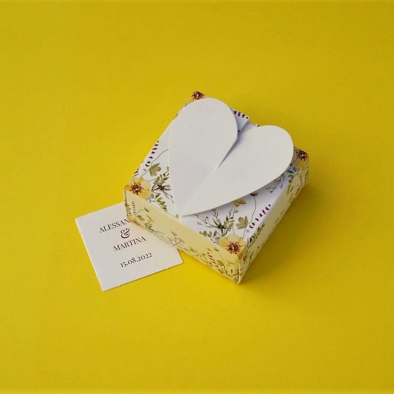Bomboniera Floreale Lega del Filo d'Oro, in cartoncino bianco con una fantasia a fiori di campo e una romantica chiusura a cuore. Accompagnata da bigliettino personalizzabile