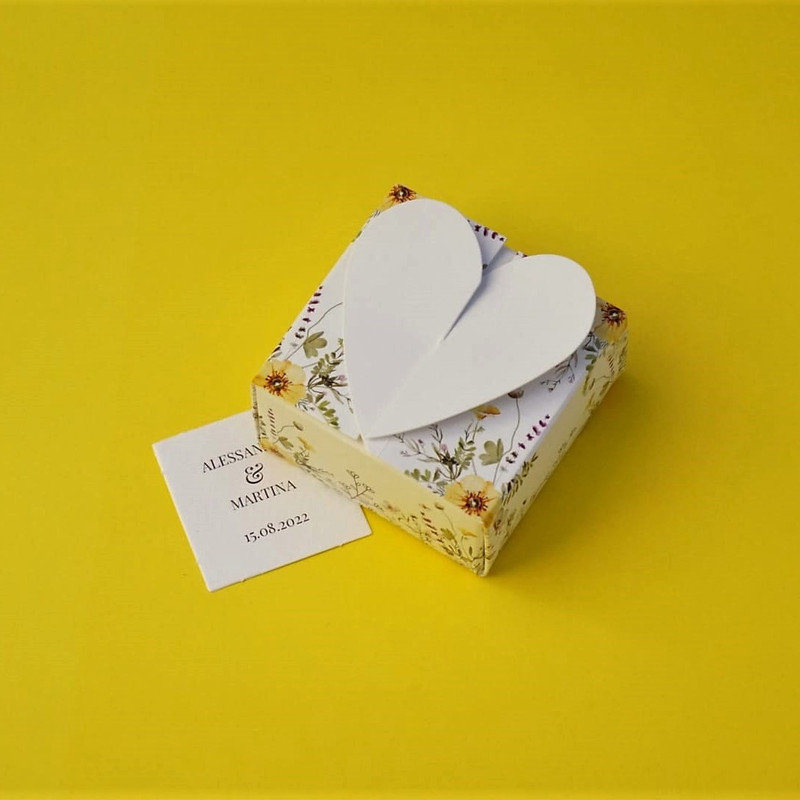 Bomboniera Floreale Lega del Filo d'Oro, in cartoncino bianco con una fantasia a fiori di campo e una romantica chiusura a cuore. Accompagnata da bigliettino personalizzabile