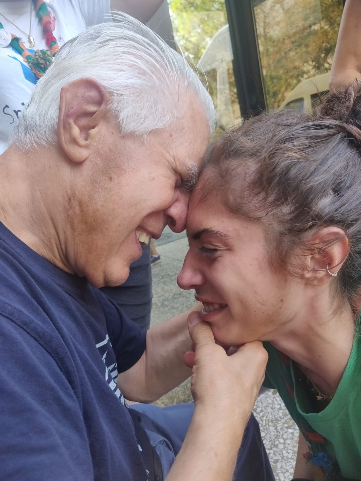 Angelo, utente anziano della Lega del Filo d'Oro, ride insieme a una volontaria scout. I due sono l'uno di fronte all'altro e le loro fronti si toccano in un momento di vicinanza ed affetto.