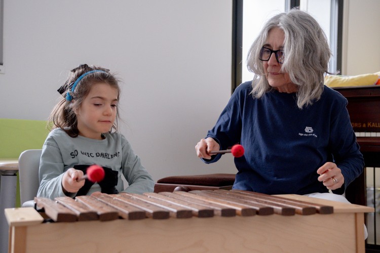 Letizia, bambina con sindrome Charge, suona un grande xilofono insieme a Fiammetta, la musicoterapista. Si trovano nell'aula di musicoterapia del Centro Nazionale, circondate di strumenti musicali.