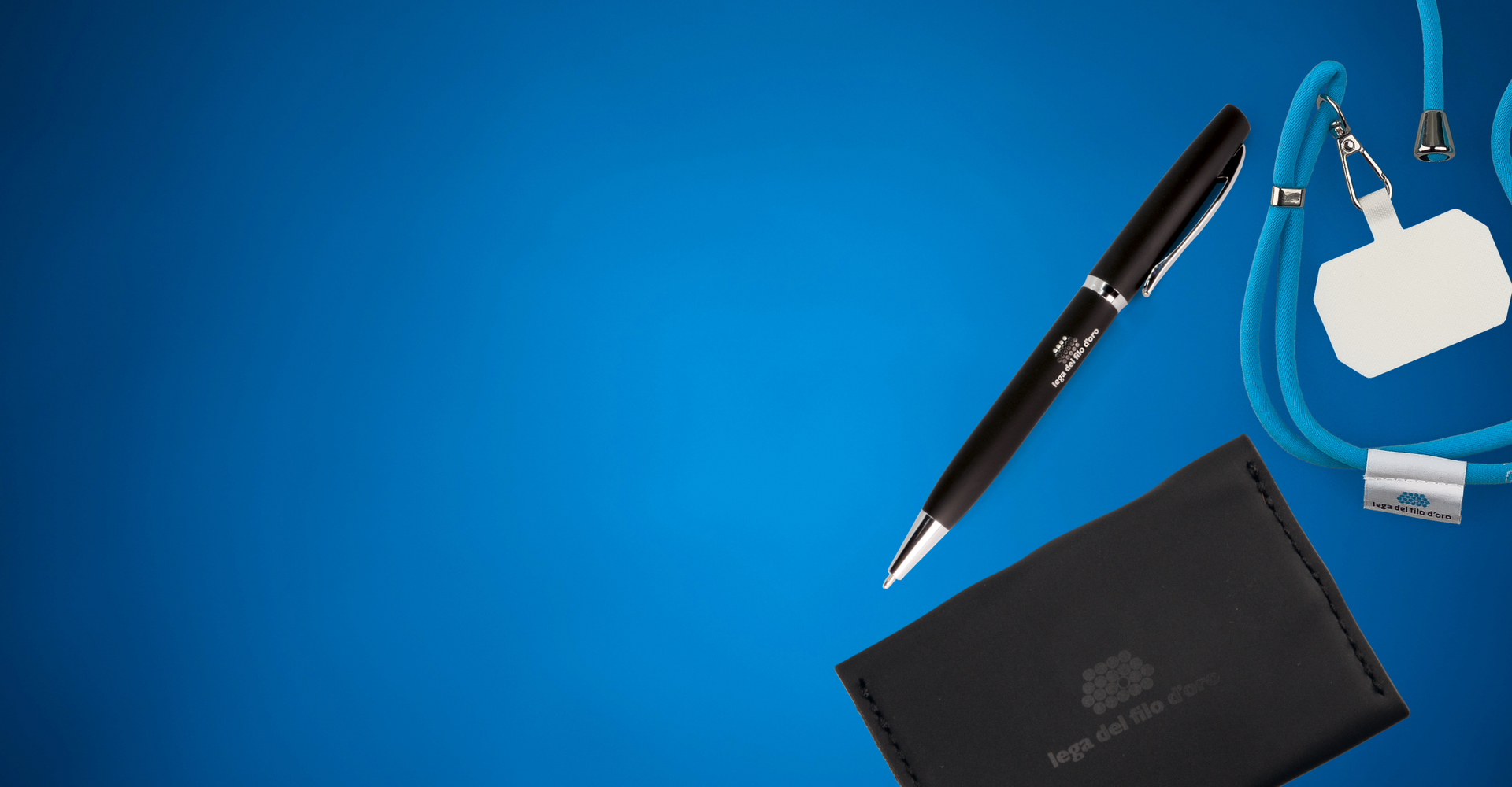 Foto su sfondo azzurro di un laccetto per smartphone, una penna e un portatessere: alcuni dei prodotti solidali ordinabili sul sito della Lega del Filo d'Oro