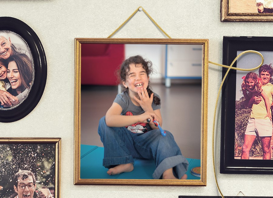 Foto di campagna sui lasciti solidali: nella foto sono presenti delle cornici con delle foto ricordo, al centro una cornice oro, con un filo oro e la foto di Giulia, bambina utente seguita dalla Lega del Filo d'Oro, seduta per terra che ride.