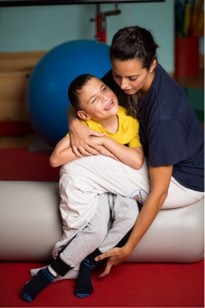 Un'operatrice della Lega del Filo d'Oro abbraccia affettuosamente un bambino, in palestra.