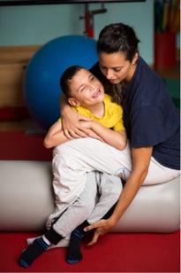 Un'operatrice della Lega del Filo d'Oro abbraccia affettuosamente un bambino, in palestra.