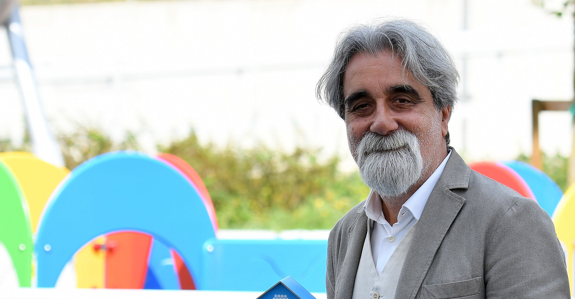 Il Maestro Beppe Vessicchio, nel parco giochi del Centro Nazionale, tiene in mano la casetta segnalino della campagna #unastoriadimani con il numero per donare via SMS solidale