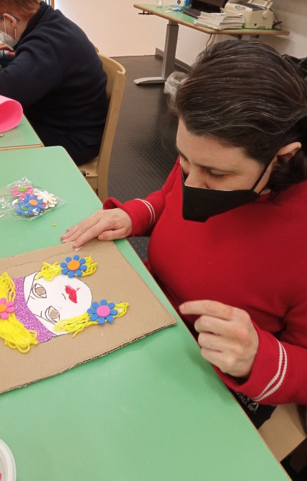 Un'ospite adulta della sede di Novara è seduta durante un laboratorio creativo e ha di fronte un disegno che rappresenta una figura femminile. 