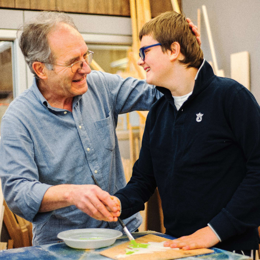 Un utente dipinge con un pennello, aiutato da un uomo che gli accarezza la testa. Entrambi sorridono.