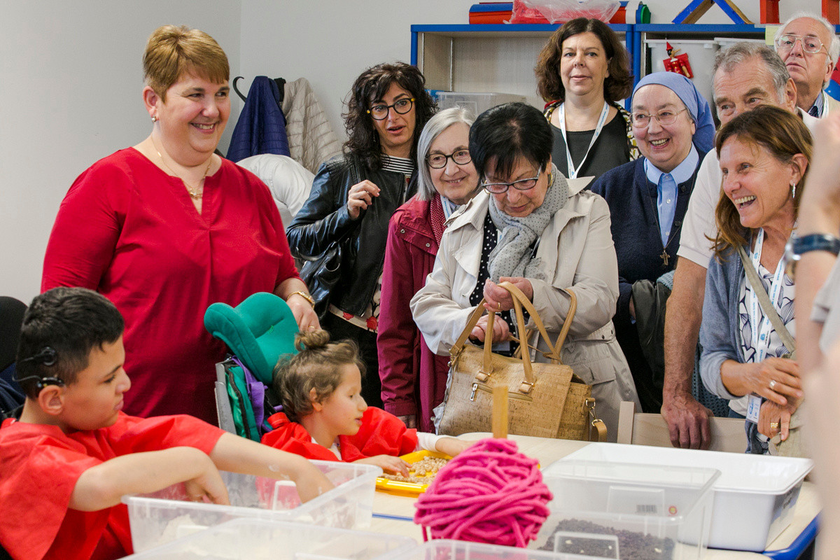 Giornata del Sostenitore - Francesco e Asia svolgono attività riabilitative con una educatrice mentre i sostenitori in visita osservano sorridendo