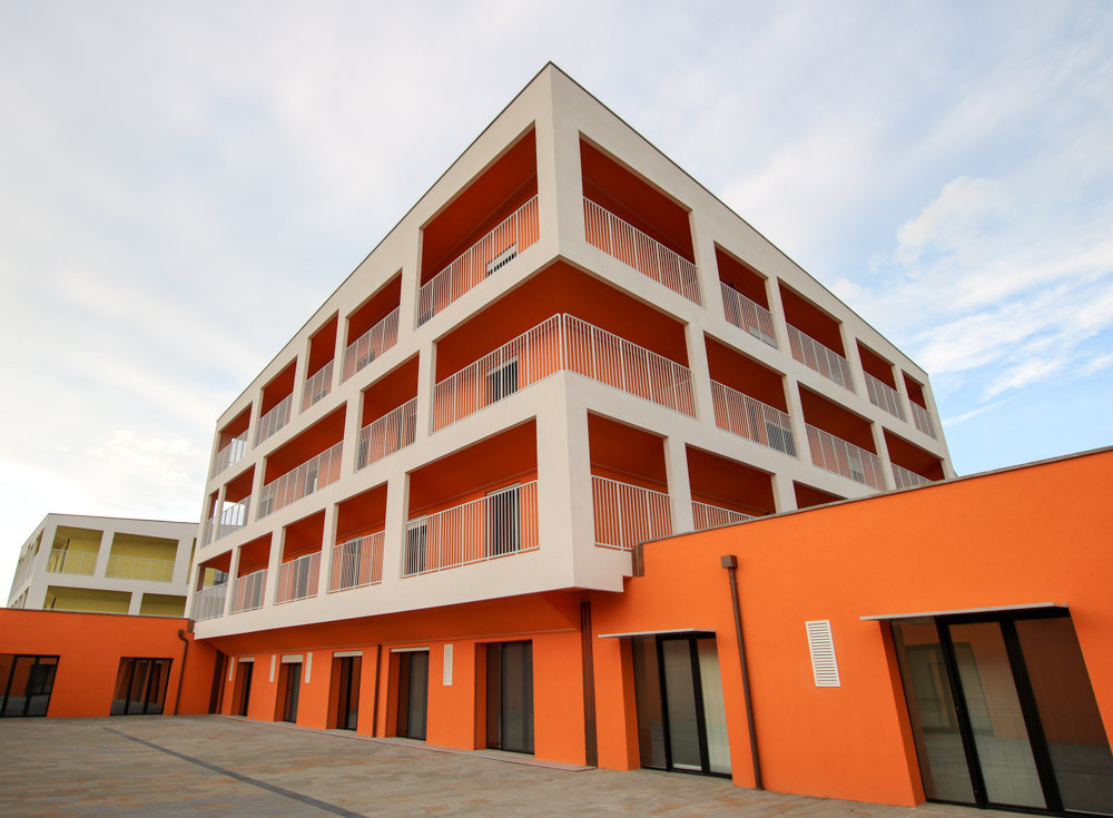 La foto inquadra un cortile del primo lotto del Centro Nazionale. Sopra di esso si eleva l'edificio arancione dedicato ai Trattamenti Intensivi