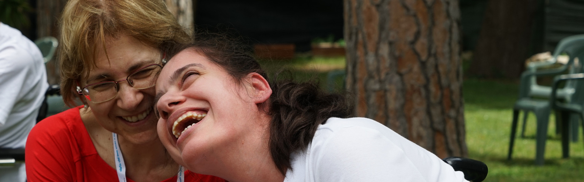 Assemblea delle Famiglie: una volontaria e una giovane utente ridono di gusto insieme guardando o ascoltando qualcosa con uno smartphone