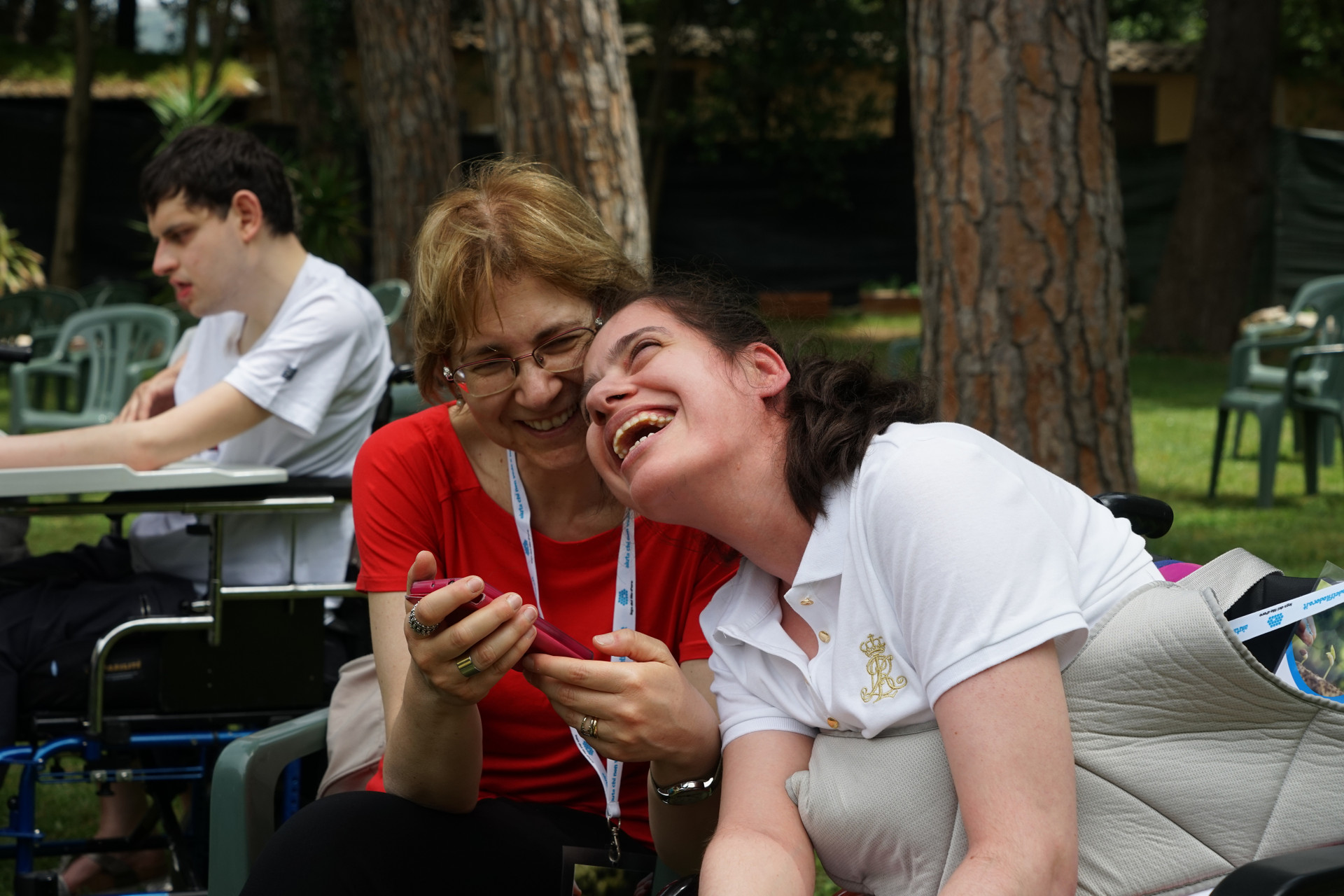 Assemblea delle Famiglie: una volontaria e una giovane utente ridono di gusto insieme ascoltando qualcosa con uno smartphone