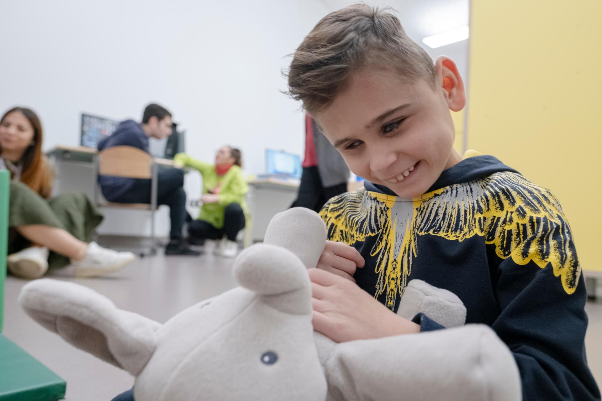Primo piano di Matteo, un bambio sordocieco. Matteo Sorride, tiene in mano un elefantino di peluches