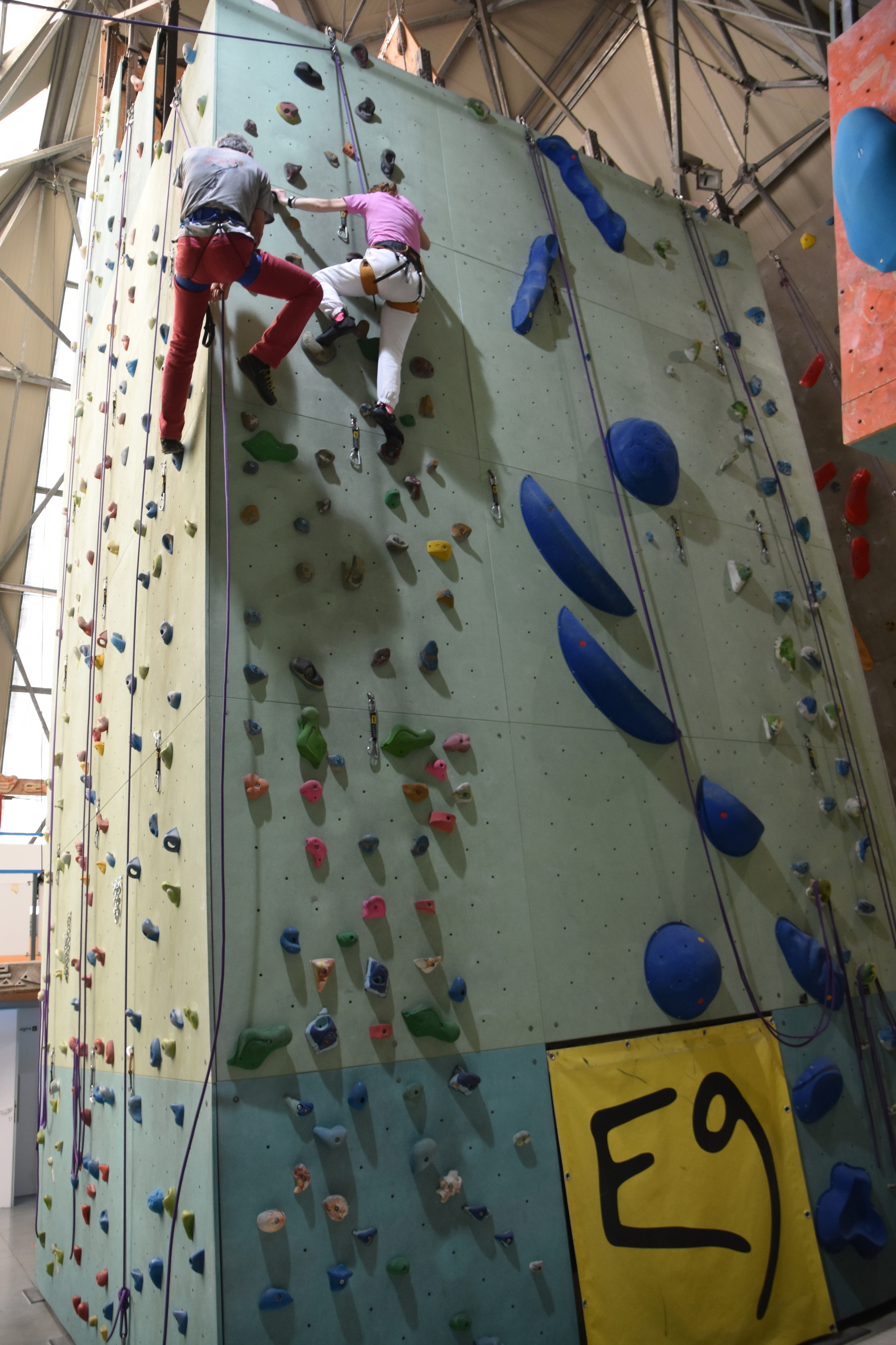 Un gruppo di persone seguite dal Servizio Territoriale di Osimo ha recentemente partecipato ad una giornata di arrampicata, con l'obiettivo di andare oltre le barriere sensoriali, sviluppare fiducia in sé stessi e socializzare. Un’utente, imbracata in sicurezza, affronta una parete da arrampicata con il supporto attento del personale della struttura.