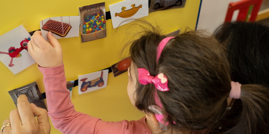 Letizia, bambina con la sindrome di Charge di circa 10 anni, sceglie la prossima attività da fare attraverso le foto che ritraggono l'attività. Vicino a lei c'è la sua educatrice.