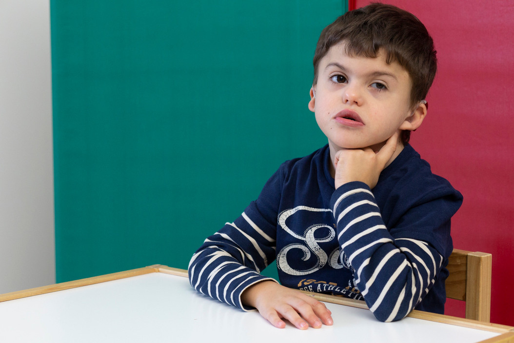 Agostino, bambino di 8 anni con sindrome di Charge, è seduto tranquillo a un banco in attesa di svolgere una attività educativa 