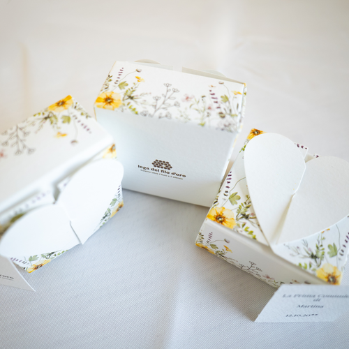 Bomboniera Floreale Lega del Filo d'Oro, in cartoncino bianco con una fantasia a fiori di campo e una romantica chiusura a cuore. Accompagnata da bigliettino personalizzabile