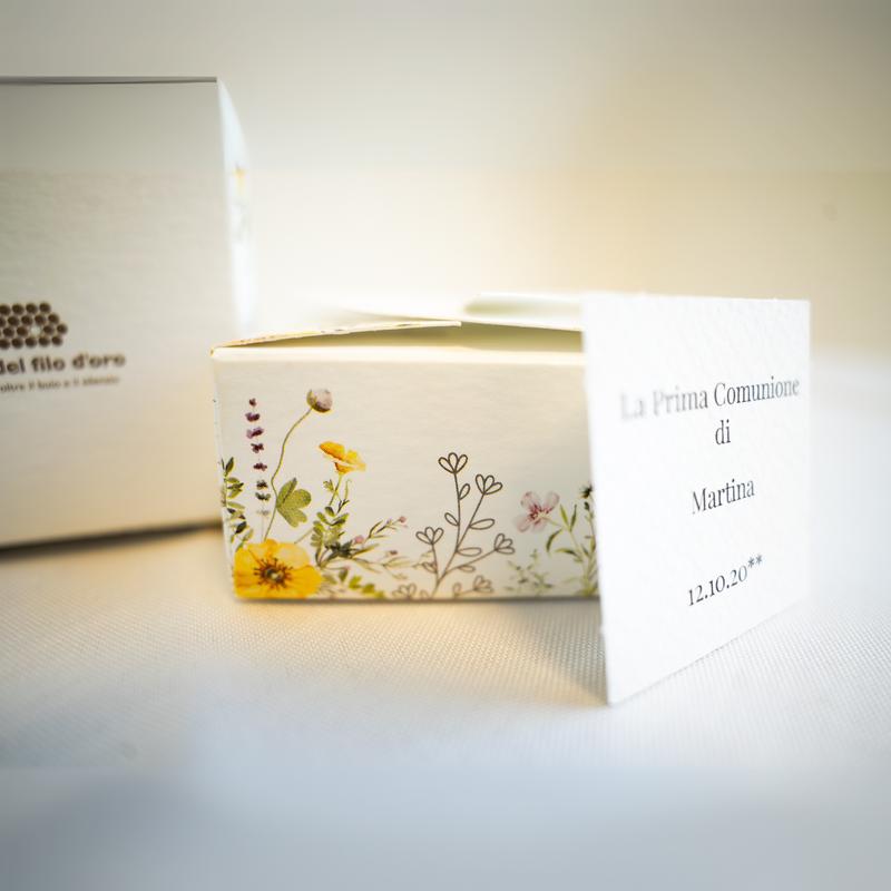 Bomboniera Floreale Lega del Filo d'Oro, in cartoncino bianco con una fantasia a fiori di campo e una romantica chiusura a cuore. Accompagnata da bigliettino personalizzabile