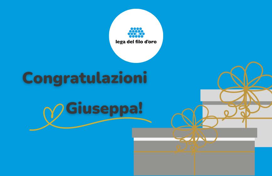L'immagine è un biglietto di congratulazioni con uno sfondo blu vivace. In alto al centro c'è il logo della "Lega del Filo d'Oro", mentre al centro è scritto in grandi lettere "Congratulazioni Giuseppa!" con un cuore e una linea decorativa dorata. In basso a destra, sono illustrati due pacchi regalo impilati, legati con nastri dorati.