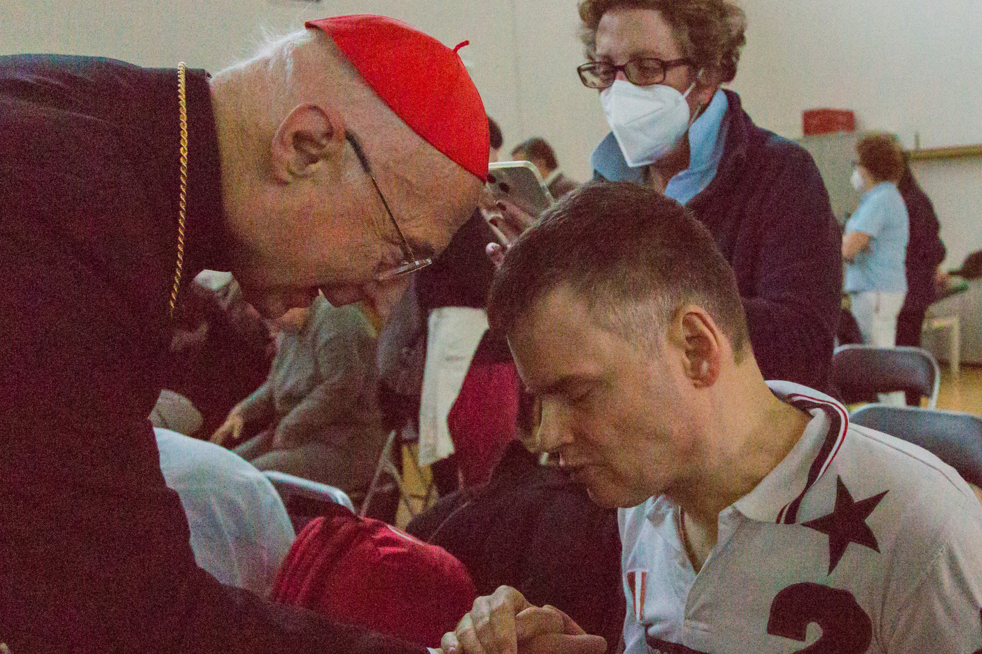 Il Cardinale Angelo Bagnasco è ritratto mentre saluta con affetto un utente della Lega del Filo d’Oro, stringendogli la mano.